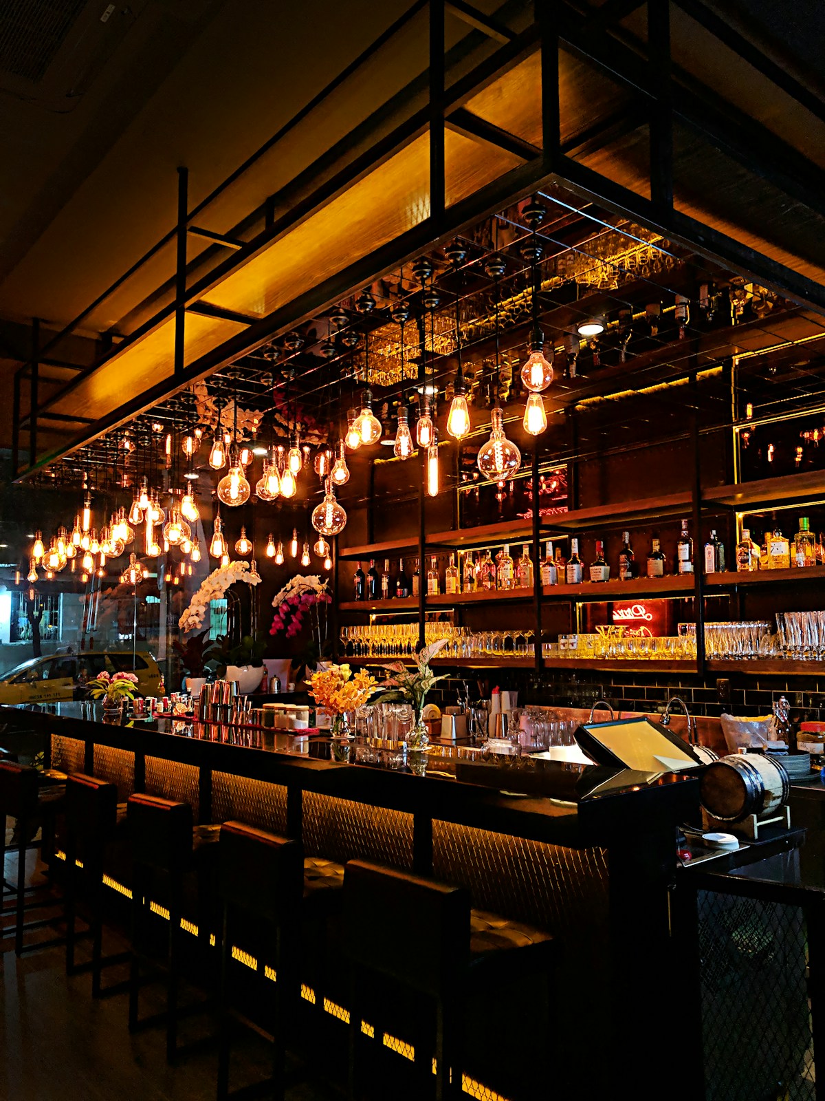 Bartender operating modern touchscreen POS behind glowing craft cocktail bar counter